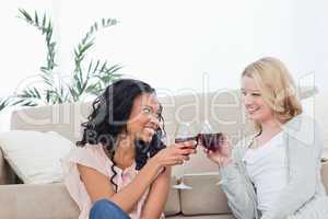 Two women smiling at each other are holding wine glasses