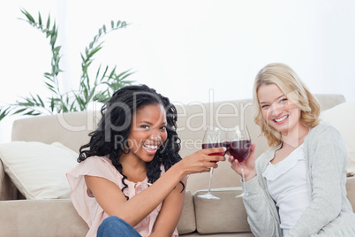 Two women sitting on the floor holding wine glasses