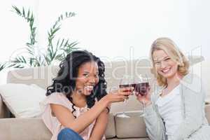 Two women sitting on the floor holding wine glasses