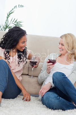 Two women are sitting on the ground leaning against a couch