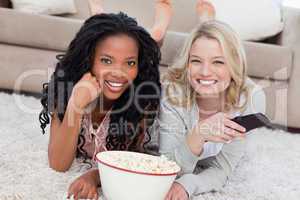 Two women lying on the ground with popcorn are smiling at the ca