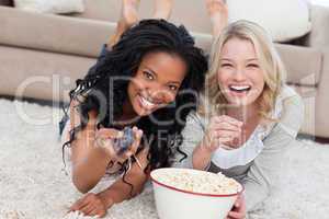 Two women lying on the ground with popcorn are smiling at the ca