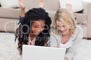 Two women are lying on the ground and looking at a laptop
