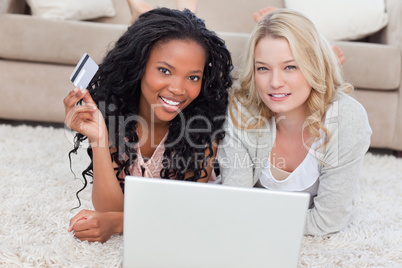 Two women looking at the camera have a laptop and a bank card