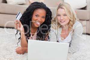 Two women looking at the camera have a laptop and a bank card