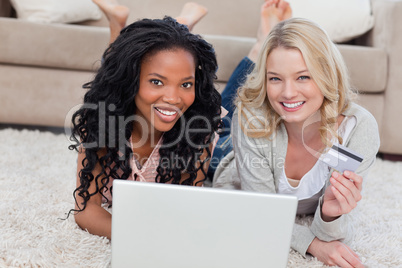 Two women are smiling at the camera with a laptop in front of th
