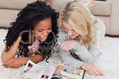 Two women lying on the floor are reading a magazine