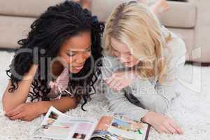 Two women lying on the floor are reading a magazine
