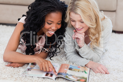 A woman is pointing at a magazine with her friend beside her