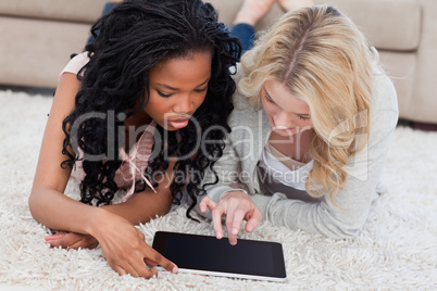 Two women are lying on the floor looking at a tablet