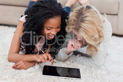 Two women are lying on the floor using a tablet