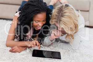 Two women are lying on the floor using a tablet