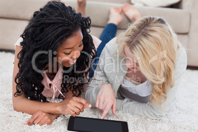 A woman lying next to her friend is pointing at a tablet