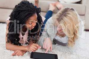 A woman lying next to her friend is pointing at a tablet