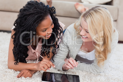 Two women lying down are looking at each other with a tablet in