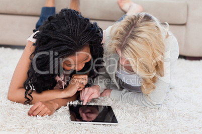 A woman is lying on the floor using a tablet computer while her