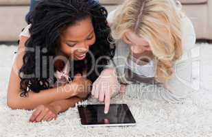 Two women lying on carpet are looking at a tablet