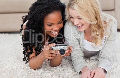 Two women lying on the floor are looking at photos on a digital