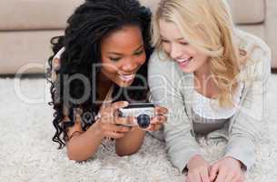 Two women lying on the floor are looking at photos on a digital