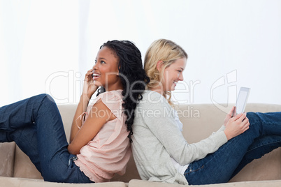 Two women sitting back to back on a couch