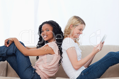 Two happy women are sitting on a couch back to back