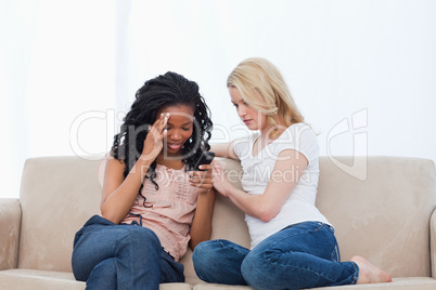 Two women sitting on a couch are looking at a mobile phone