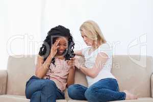 Two women sitting on a couch are looking at a mobile phone