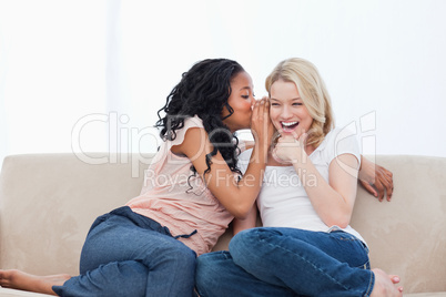 A woman is whispering into her smiling friends ear