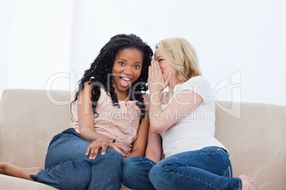 A woman is whispering into her surprised friends ear