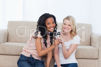 Two women sitting on the floor are holding a microphone