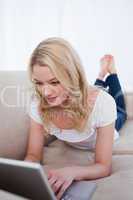 A woman lying on a couch is typing on her laptop