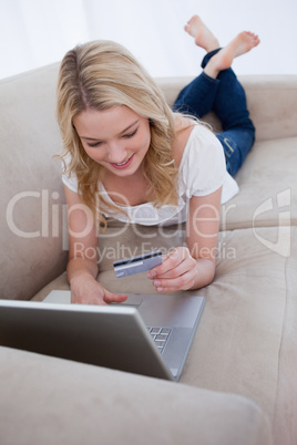 A woman lying on a couch with a laptop in front of her is lookin