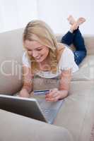 A smiling woman typing on her laptop is holding a bank card