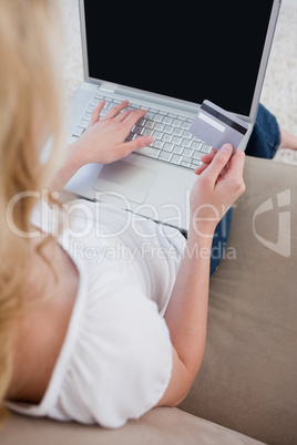 Overhead view of a woman holding a bank card and typing on a lap
