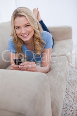 A smiling woman looking at the camera is holding a mobile phone