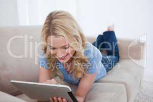 A smiling woman lying on a couch is using her tablet