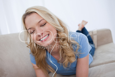 A woman lying on a couch is listening to music with earphones