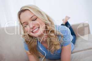 A woman lying on a couch is listening to music with earphones