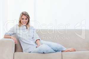 A woman smiling at the camera is sitting on a couch