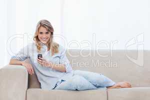 A woman sitting on a couch holding a mobile phone is smiling