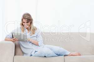 A smiling woman holding a tablet is sitting on a couch