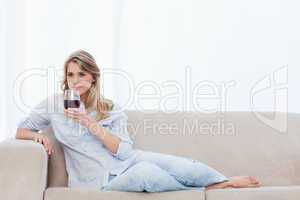 A woman lying on a couch is holding a glass of red wine