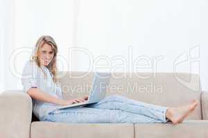 A woman lying down on a couch has a laptop on her legs