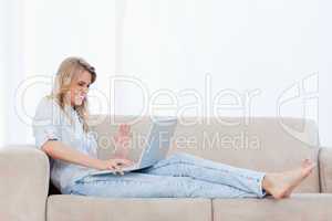 A happy woman sitting on a couch is using her laptop