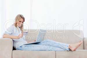 A woman lying on a couch with a laptop in front of her is holdin