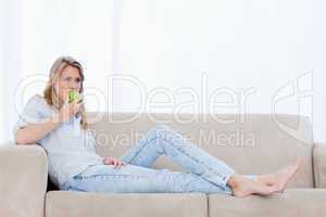A woman lying on a couch is eating an apple