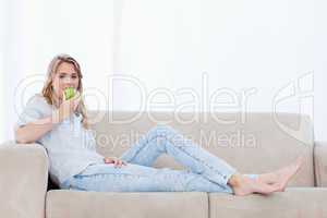 A woman eating an apple is lying on a couch