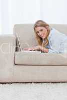 A woman lying on a couch is using a laptop