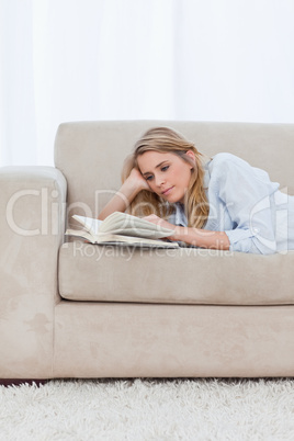 A woman lying on a couch resting her head on her hand is reading