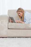 A smiling woman is lying on a couch using a tablet